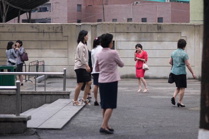 Pedestrians use mobile phones outside a subway station in Pyongyang on June 19, 2019.