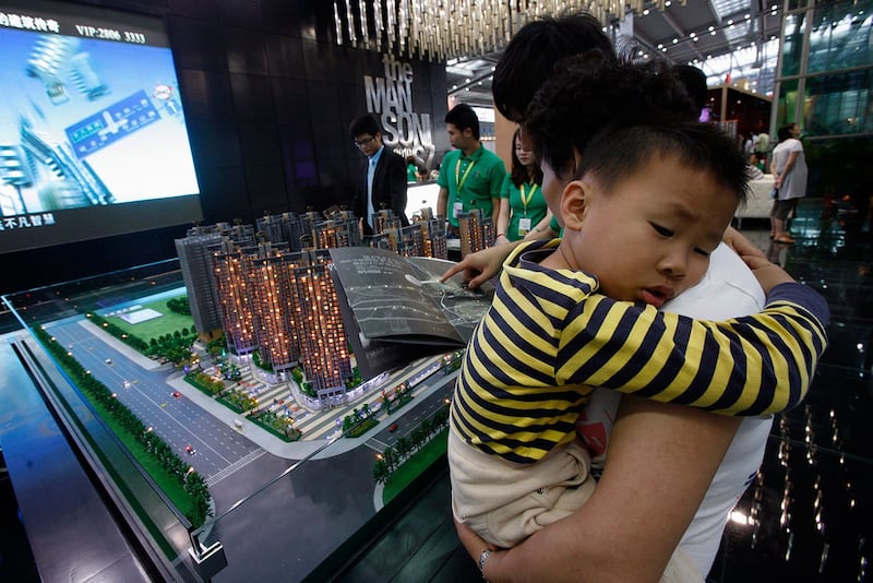 在深圳房地产博览会上,一名参观者抱着一个孩子正在查看宣传册。(路透社)