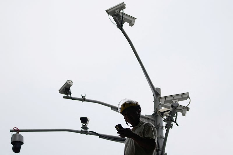 A man looks at a phone as he walks under surveillance cameras on a street, in Shanghai, Sept. 27, 2023.